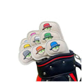Set of cream-colored Malbon-style golf iron headcovers featuring cartoon faces with multi-colored bucket hats (red, blue, green, orange, gray, yellow, pink); shown inserted in black/red golf bag with strong magnetic closure system.