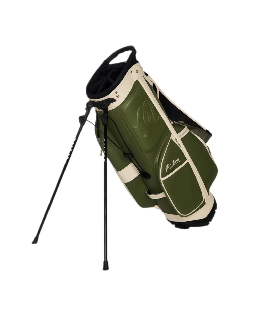 Malbon Artigianale golf bag standing upright on its dual support legs; durable construction with ergonomic handle and sleek olive green and cream finish.