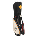 Front view of Malbon Golf caddie bag in black and cream PU leather with orange trim, featuring a cartoon golf ball character wearing a cap, "Malbon" script logo, and durable shoulder strap.