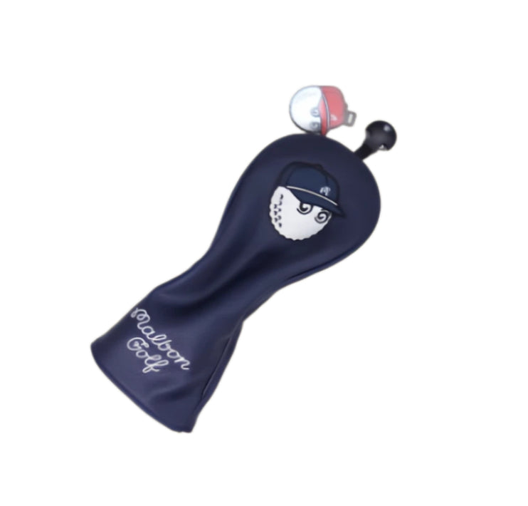 Angled view of navy Malbon golf headcover highlighting the curved fit over a driver, embroidered “Malbon Golf” text, and detachable red-capped cartoon ball magnet accessory.