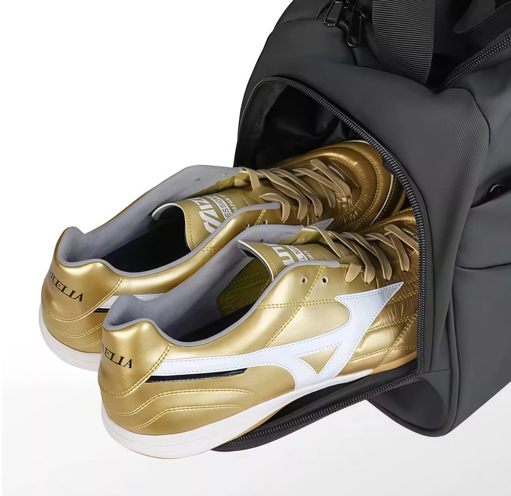 Close-up interior view of the Mizuno 39L Black Duffel Bag’s dedicated single-sided isolated shoe compartment containing a pair of shiny gold Mizuno Morelia soccer cleats, demonstrating smart organization to keep dirty footwear separate from clean gear.