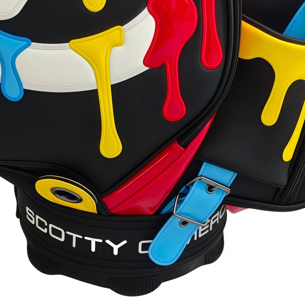 A macro close-up of the Scotty Cameron 2025 Paint Drip Tour Bag. This shot details the raised texture of the red, yellow, and blue paint drip graphics, the blue leather strap, and the white "SCOTTY CAMERON" embroidery at the base.