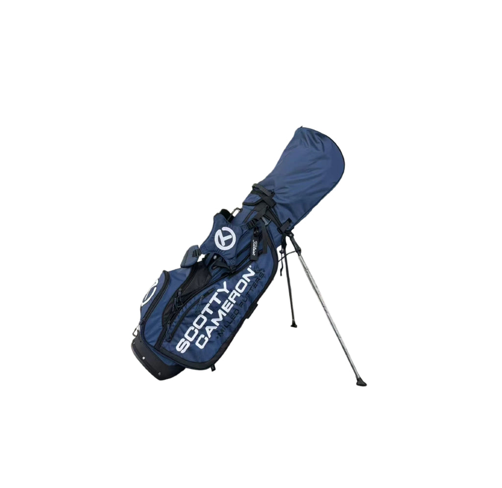 Angled view of the Scotty Cameron Pathfinder Mainstay Stand Bag in Navy Blue. This lightweight carry bag features a prominent white Circle T logo, "SCOTTY CAMERON MILLED PUTTERS" branding, and a durable dual-strap system.