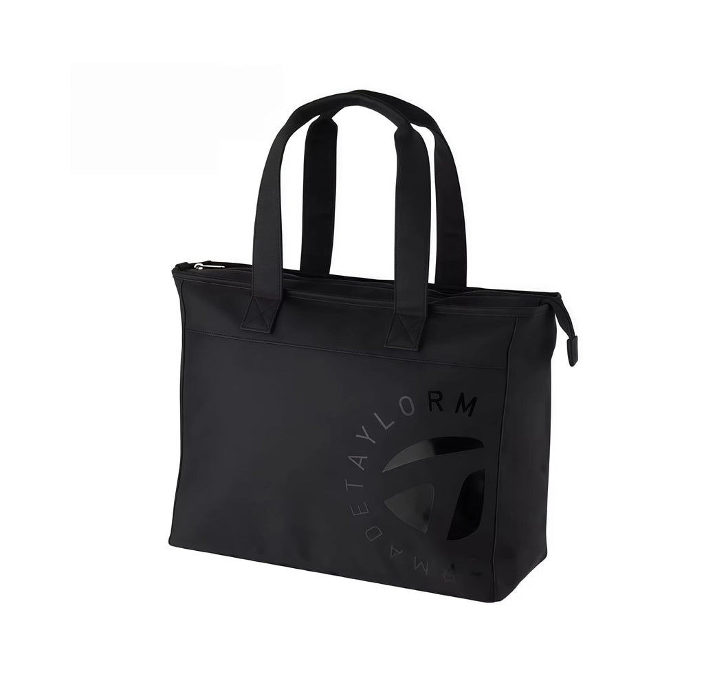 Front view of the TaylorMade Black Golf Tote featuring a subtle tonal "T" logo and circular "TAYLORMADE" text. Includes dual top handles and zippered closure for secure storage.
